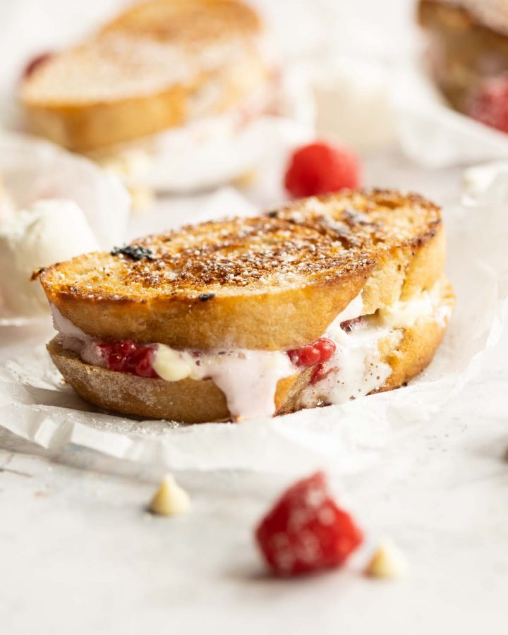 sandwich on crumpled parchment paper surrounded by raspberries and white chocolate chips