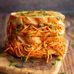 two spaghetti sandwiches stacked on each other on chopping board garnished with parsley