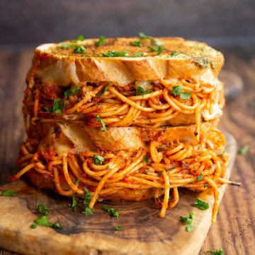 two spaghetti sandwiches stacked on each other on chopping board garnished with parsley