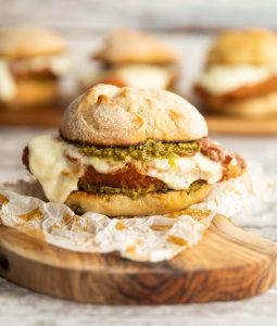 chicken pesto sandwich on wooden board with 3 more sandwiches blurred in background