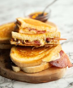 4 bacon grilled cheese halves on wooden board with small glass pot of maple syrup