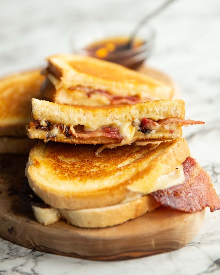 4 bacon grilled cheese halves on wooden board with small glass pot of maple syrup