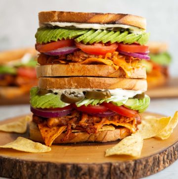 two nacho chicken sandwiches stacked on top of each other on wooden board with more blurred in background