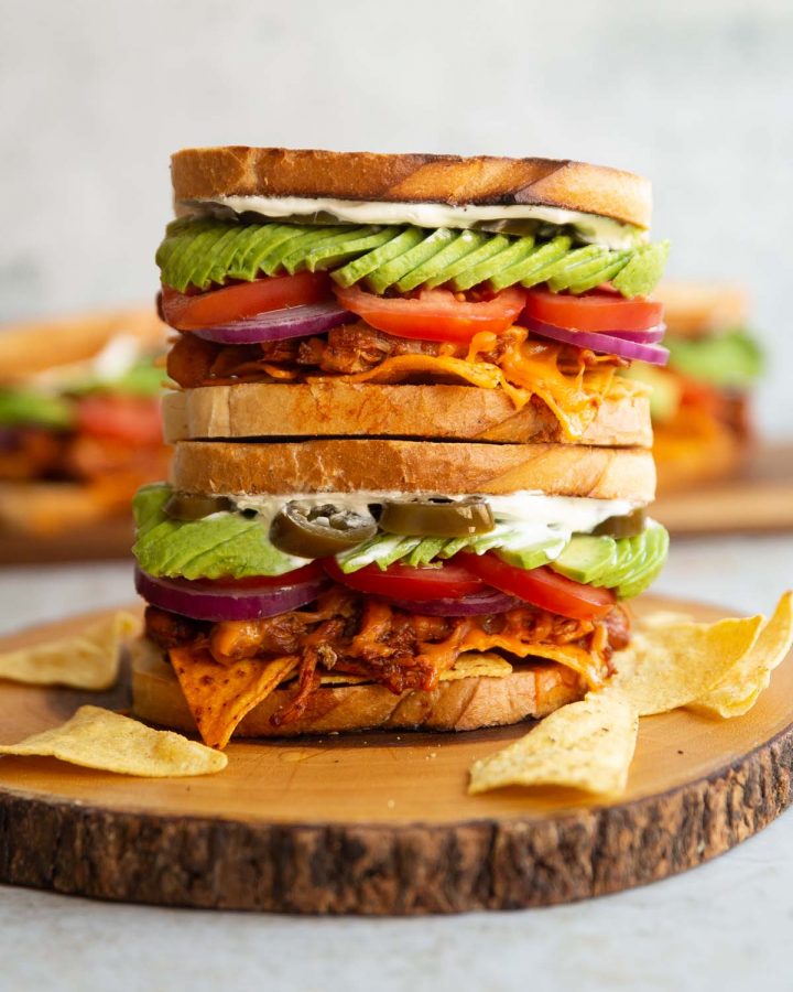 two nacho chicken sandwiches stacked on top of each other on wooden board with more blurred in background