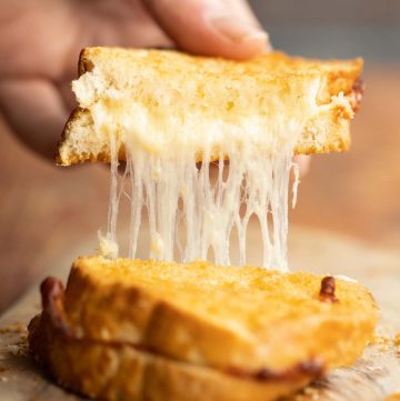 close up shot of hand pulling up half of grilled cheese with cheese dripping out