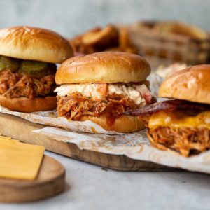 3 pulled chicken sandwiches on crumpled paper on chopping board