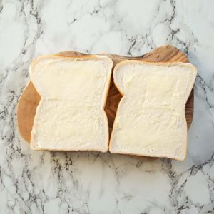 over head shot of two slices of buttered bread on chopping board