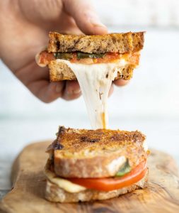 hand lifting half of caprese sandwich with cheese dripping out