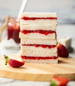 4 jam finger sandwiches stacked on each other on chopping board surrounded by strawberries