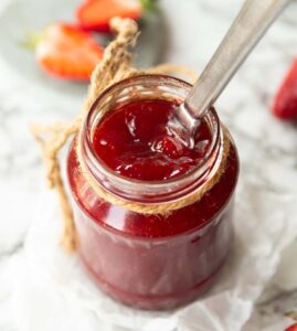 close up shot of strawberry jam in jam jar with silver knife digging in