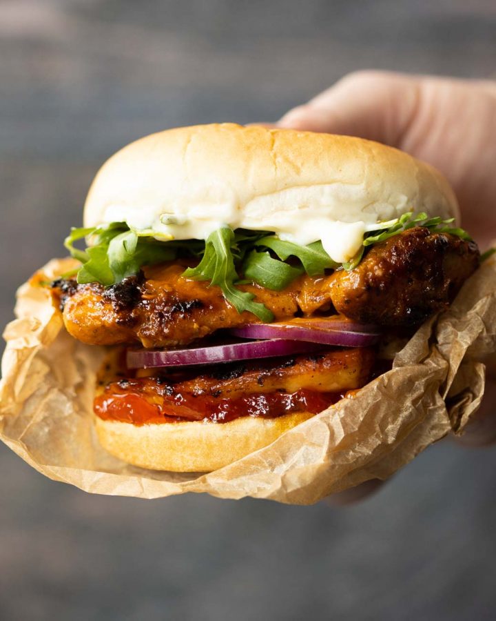 close up shot of hand holding peri peri chicken sandwich in brown wrapper