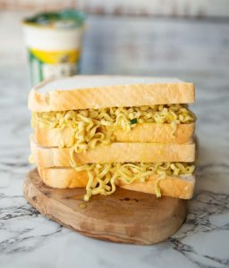 two pot noodle sandwiches stacke don each other with pot noodle blurred in background