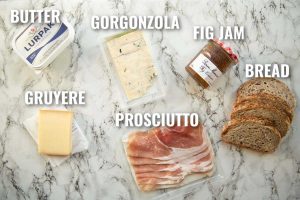 overhead shot of prosciutto grilled cheese ingredients on marble backdrop with text labels