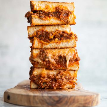 4 sloppy joe grilled cheese halves stacked on each other on wooden board