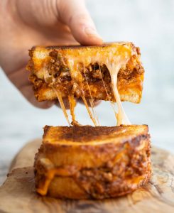 close up shot of hand lifting half of sloppy joe grilled cheese showing cheesy filling