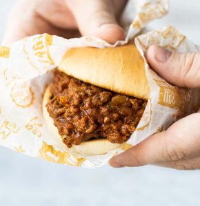 close up shot of hands holding sloppy joe wrapped in paper
