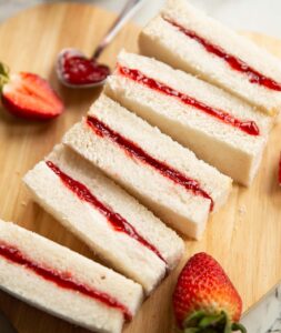 5 finger jam sandwiches on small chopping board with silver spoon and two strawberries