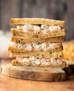 3 prawn mayonnaise sandwiches stacked on each other on wooden chopping board
