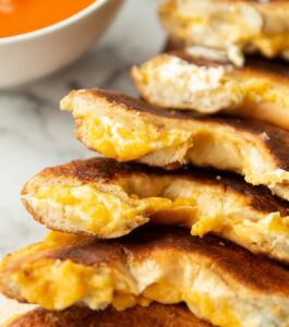 close up shot of halved bagel grilled cheese with bowl of soup blurred in background