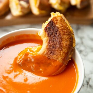 half a bagel grilled cheese in a small bowl of tomato soup with more sliced in the background