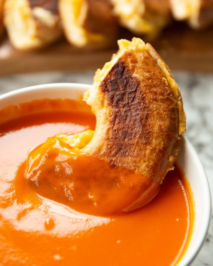 half a bagel grilled cheese in a small bowl of tomato soup with more sliced in the background