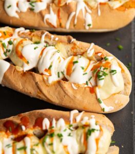close up shot of 3 buffalo chicken meatball subs on black baking tray