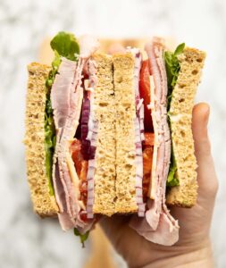 close up overhead shot of hand holding 2 cold ham sandwich halves showing filling