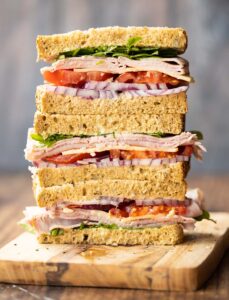 3 ham sandwich halves stacked on each other on wooden chopping board
