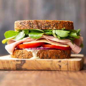 close up shot of ham sandwich on wooden board with wooden backdrop