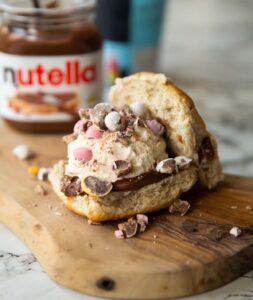 close up shot of hot cross bun ice cream sandwich on small chopping board with ice cream and nutella blurred in background