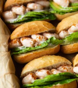 close up shot of prawn cocktail sandwiches lined up in dish with brown parchment paper