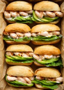 overhead shot of 8 prawn cocktail sandwiches in dish with brown parchment paper