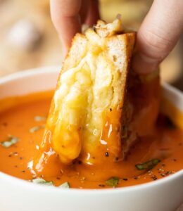 close up shot of hand dunking roasted garlic grilled cheese into tomato soup