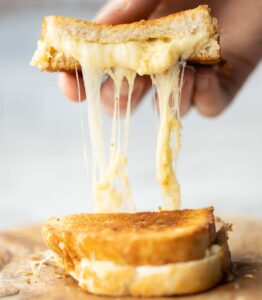 hand lifting half of roasted garlic grilled cheese with cheese dripping out