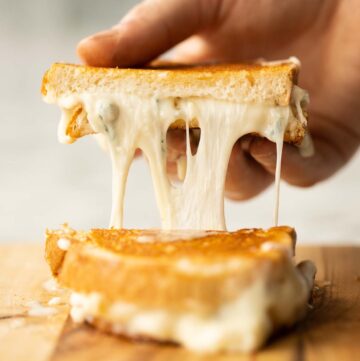 hand lifting half a grilled cheese with cheese oozing out