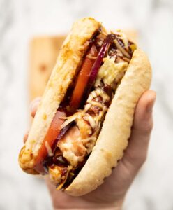 close up overhead shot of hand holding hunters chicken sandwich above marble background