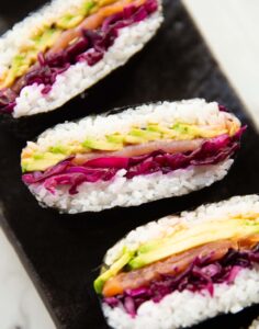 close up shot of 3 salmon sushi sandwiches on black serving plate