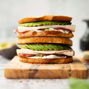 2 turkey avocado sandwiches stacked on each other on wooden chopping board