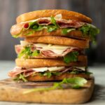 3 salami sandwiches stacked on each other on wooden chopping board